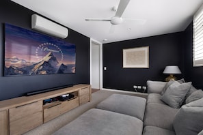A modern living room with a flat-screen TV, a ceiling fan, a framed artwork, and a sofa.
