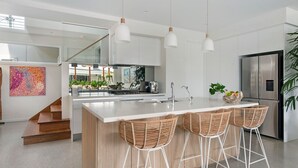 A modern kitchen with a central island, white cabinetry, stainless steel appliances, and a glass staircase.