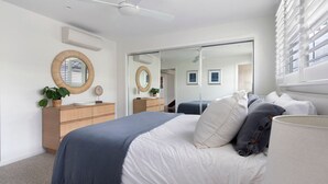 A modern bedroom with a large bed, a dresser, a mirror, and a sliding door closet.