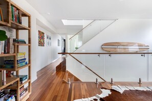 A modern interior with wooden flooring, a glass staircase, and a bookshelf filled with books. - Luxury Tri-Level Duplex in Mermaid Beach (Mermaid Beach)
