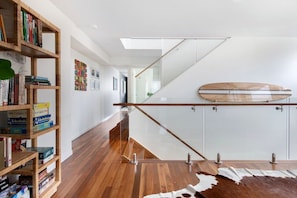A modern interior with a wooden bookshelf, a glass staircase, and a cowhide rug. - Luxury Tri-Level Duplex in Mermaid Beach (Mermaid Beach)
