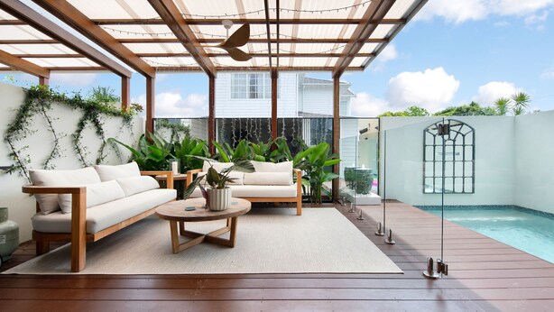 A covered outdoor seating area with a pool, wooden deck, and potted plants.