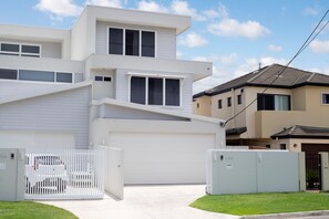 A modern multi-story residential building with a garage, a white picket fence, and a well-maintained lawn. - Luxury Tri-Level Duplex in Mermaid Beach (Mermaid Beach)