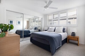 A bedroom with two beds, a ceiling fan, a mirror, and a window with blinds. - Luxury Tri-Level Duplex in Mermaid Beach (Mermaid Beach)