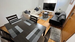 Un comedor con mesa y sillas, un sofá, un televisor y una mesita auxiliar.
