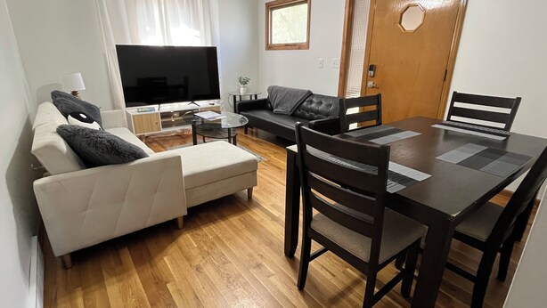 Una sala de estar con sofá, reposapiés, televisor, mesa de centro y mesa de comedor con sillas.