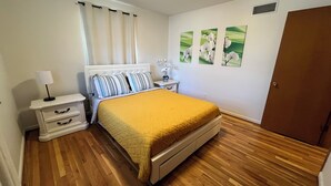 Un dormitorio con cama, mesitas de noche, lámpara, puerta y decoración en la pared.