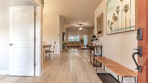 Un pasillo amplio con un banco de madera, una zona de comedor con sofá y una cocina con mesa y sillas de madera.