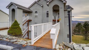 A two-story house with a wooden deck, white railings, and a stone wall. - Cozy Condo w/ Balcony & Views in Beech Mountain! (Beech Mountain)