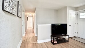 A hallway with a white radiator, a black TV stand with a flat-screen TV, and two wall-mounted decorative pieces.