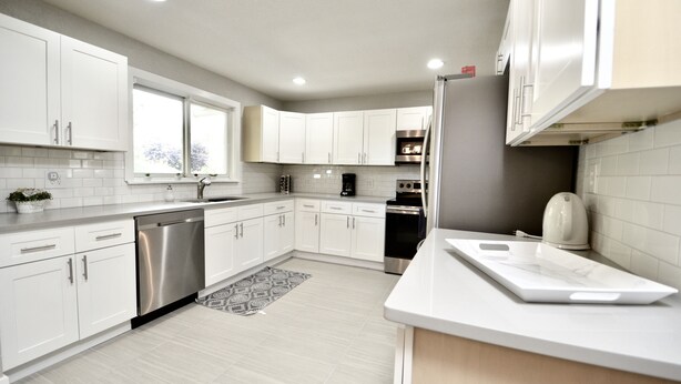 A modern kitchen with white cabinets, stainless steel appliances, and a large window.