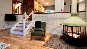 Ein Wohnzimmer mit Kamin, einer Treppe und einer dahinterliegenden Küche.