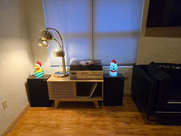 A room with a wooden floor, a desk with a lamp, a stereo system, and two small speakers.
