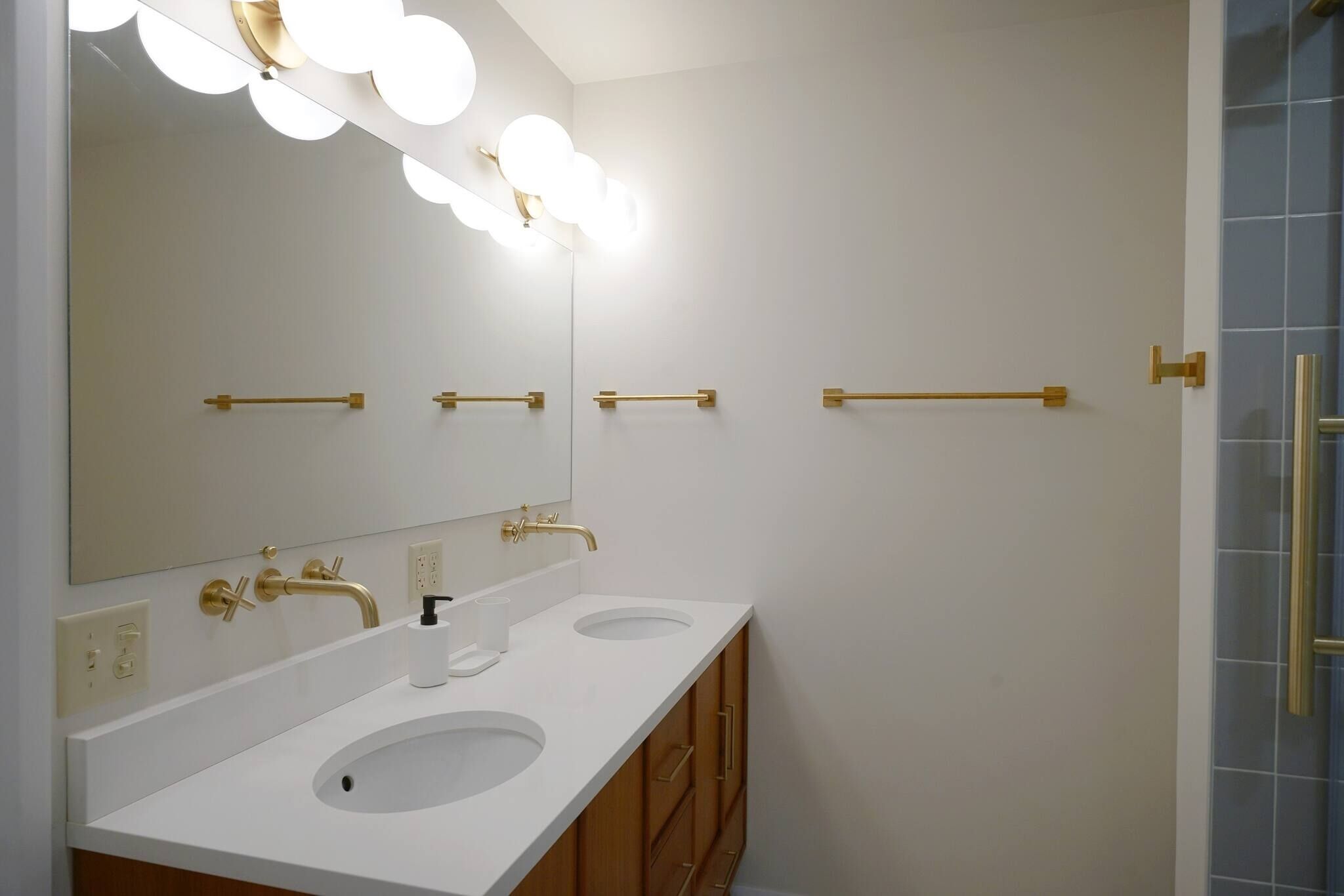 A bathroom with two sinks, a large mirror with lights, and a shower area.