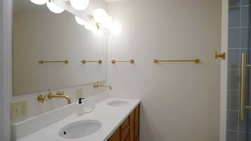 A bathroom with two sinks, a large mirror with lights, and a shower area.