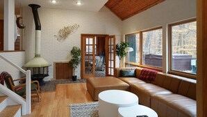 Ein gemütliches Wohnzimmer mit Kamin, Holzbalken, einer Couch und großen Fenstern.