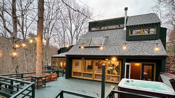 Eine Hütte mit einer Terrasse, einem Whirlpool und einem großen Fenster mit Blick auf einen Wald.