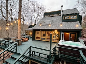 A cabin with a deck, a hot tub, and a large window overlooking a forest.