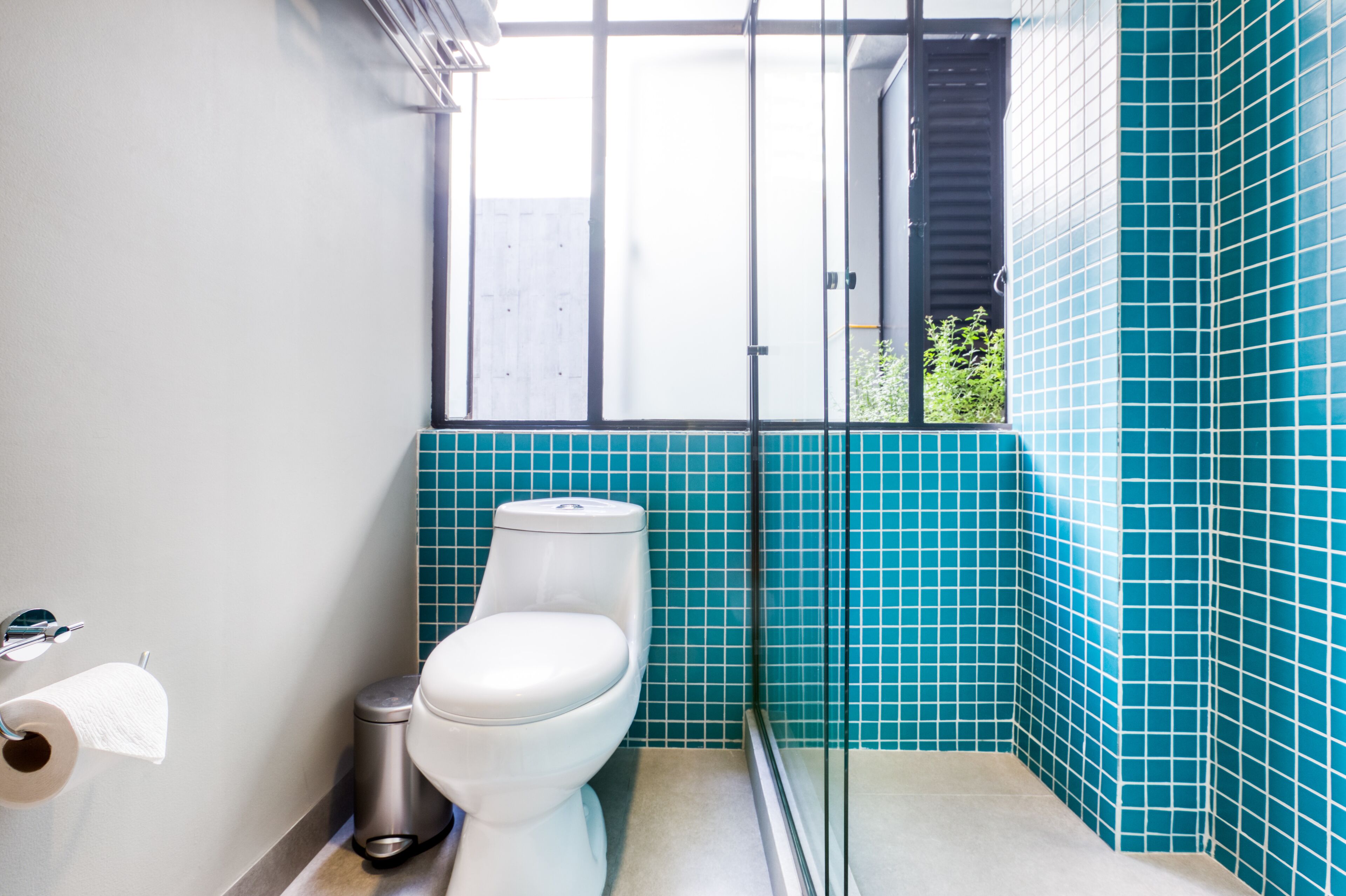A bathroom with a toilet, a trash bin, and a window.