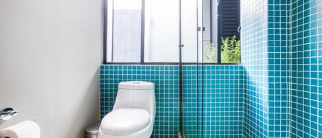 A bathroom with a toilet, a trash bin, and a window.