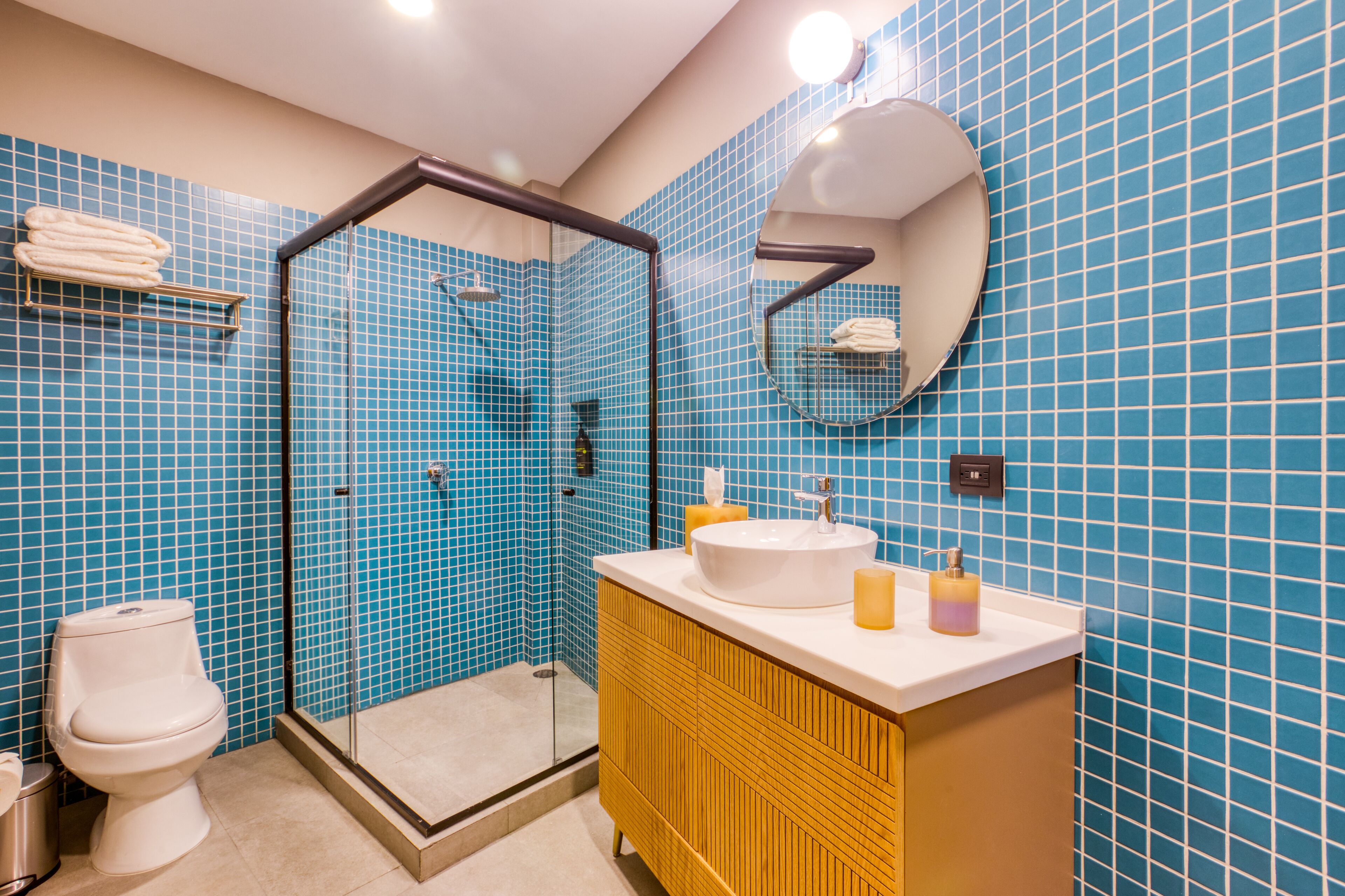 A bathroom with a glass-enclosed shower, a white toilet, a yellow vanity with a sink, and blue tiled walls.