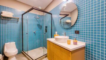 A bathroom with a glass-enclosed shower, a white toilet, a yellow vanity with a sink, and blue tiled walls.