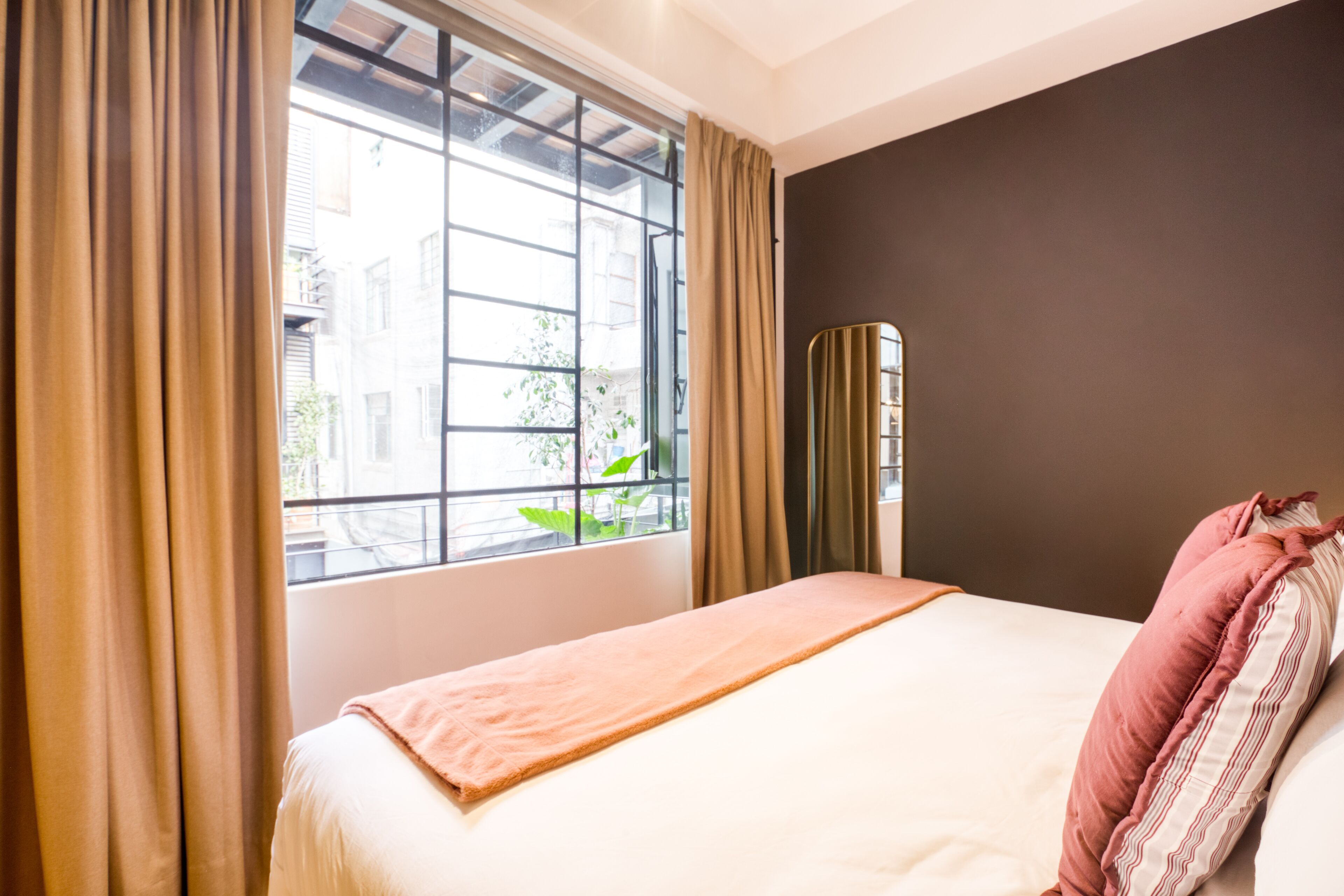 A hotel room with a bed, a window with curtains, and a view of buildings outside.