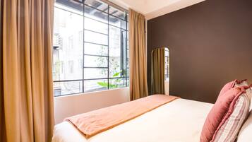 A hotel room with a bed, a window with curtains, and a view of buildings outside.
