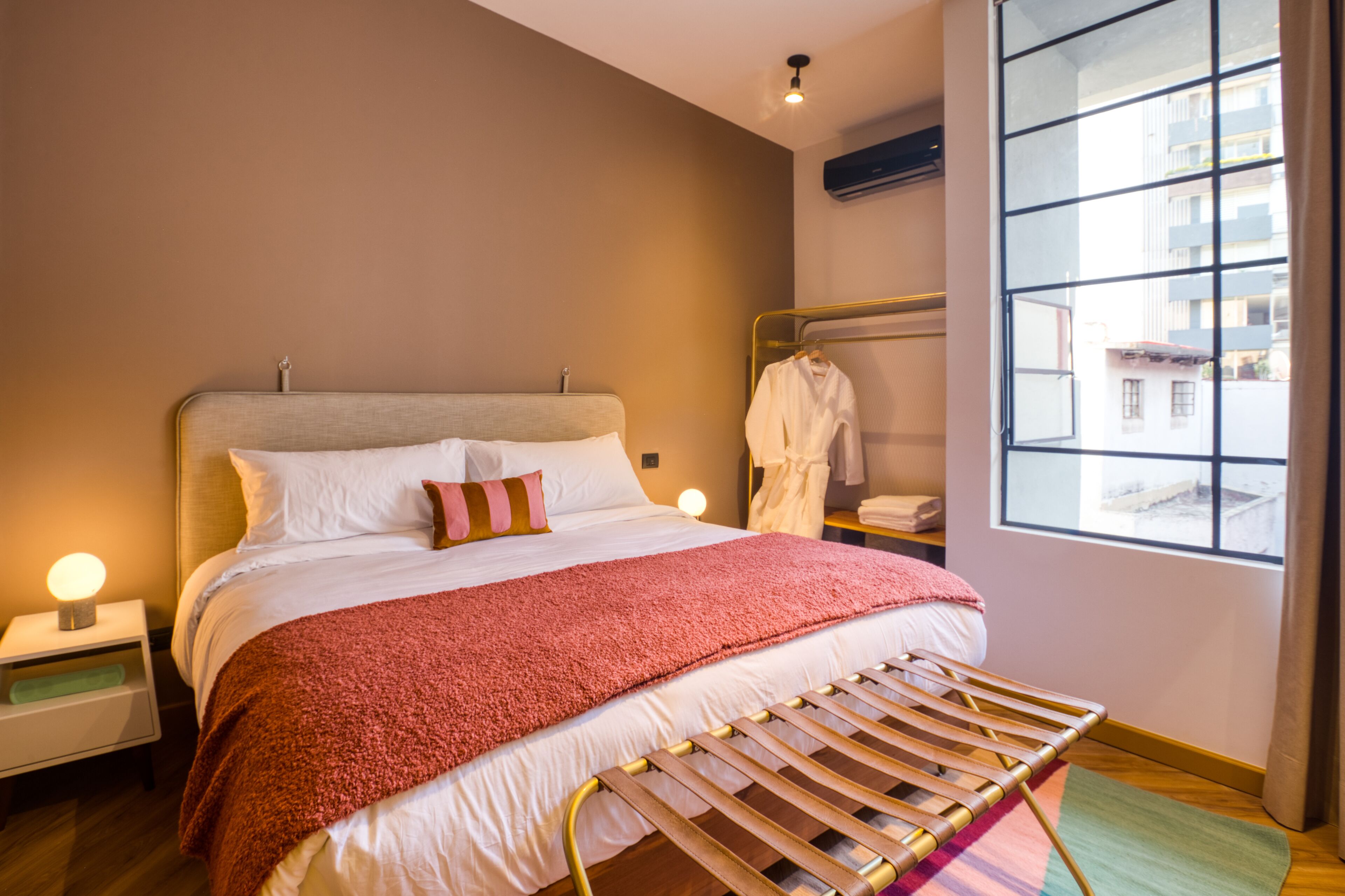 A neatly made bed with a red blanket, a bedside lamp, and a wooden chair.