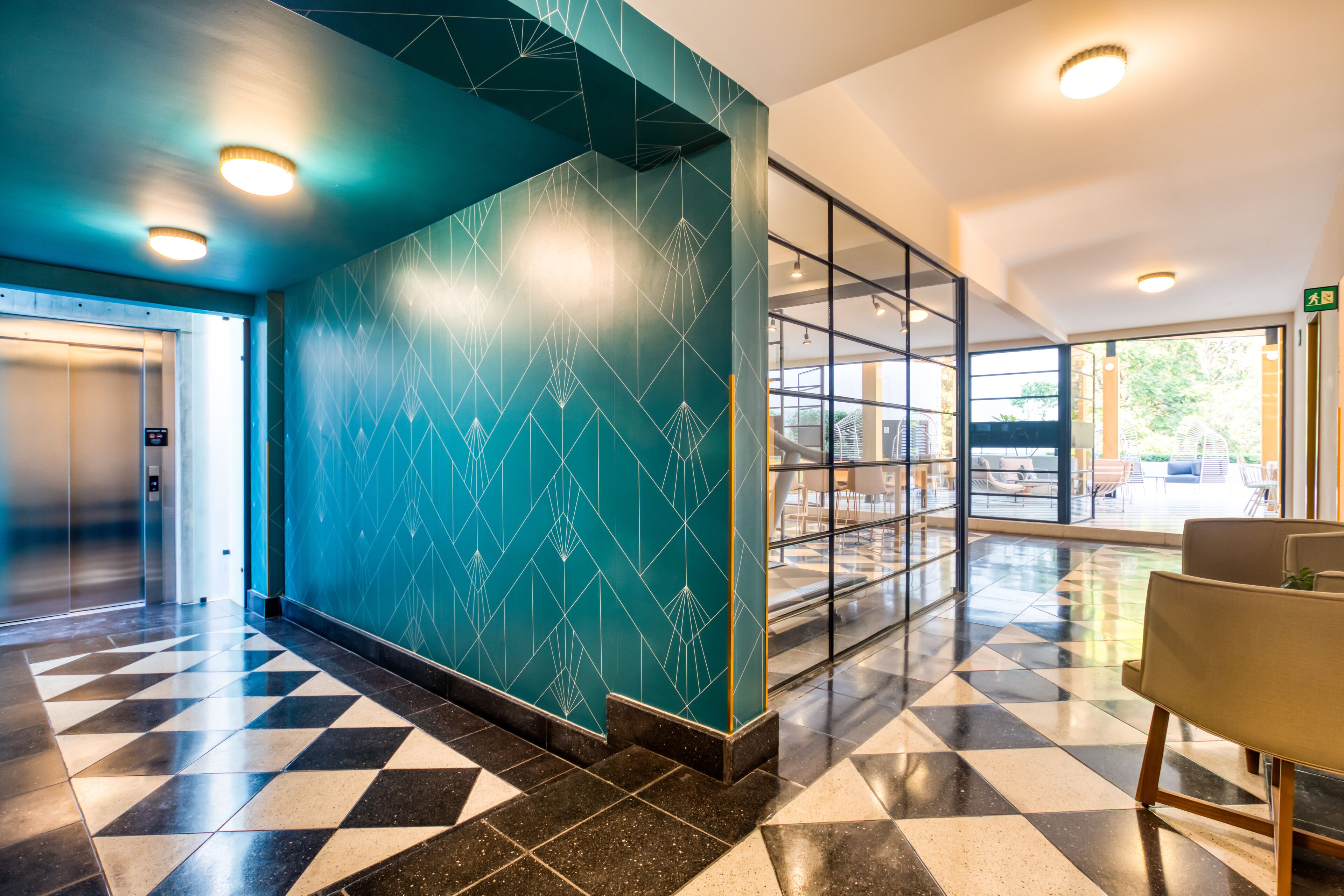 Un vestíbulo moderno con pared de diseño geométrico, suelo a cuadros y una zona de estar con separador de vidrio.