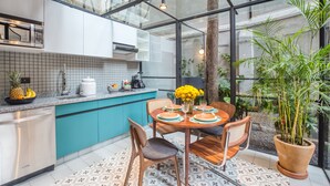 Una cocina moderna con cerramiento de vidrio, un comedor con mesa dispuesta para cuatro, y una planta grande en maceta.