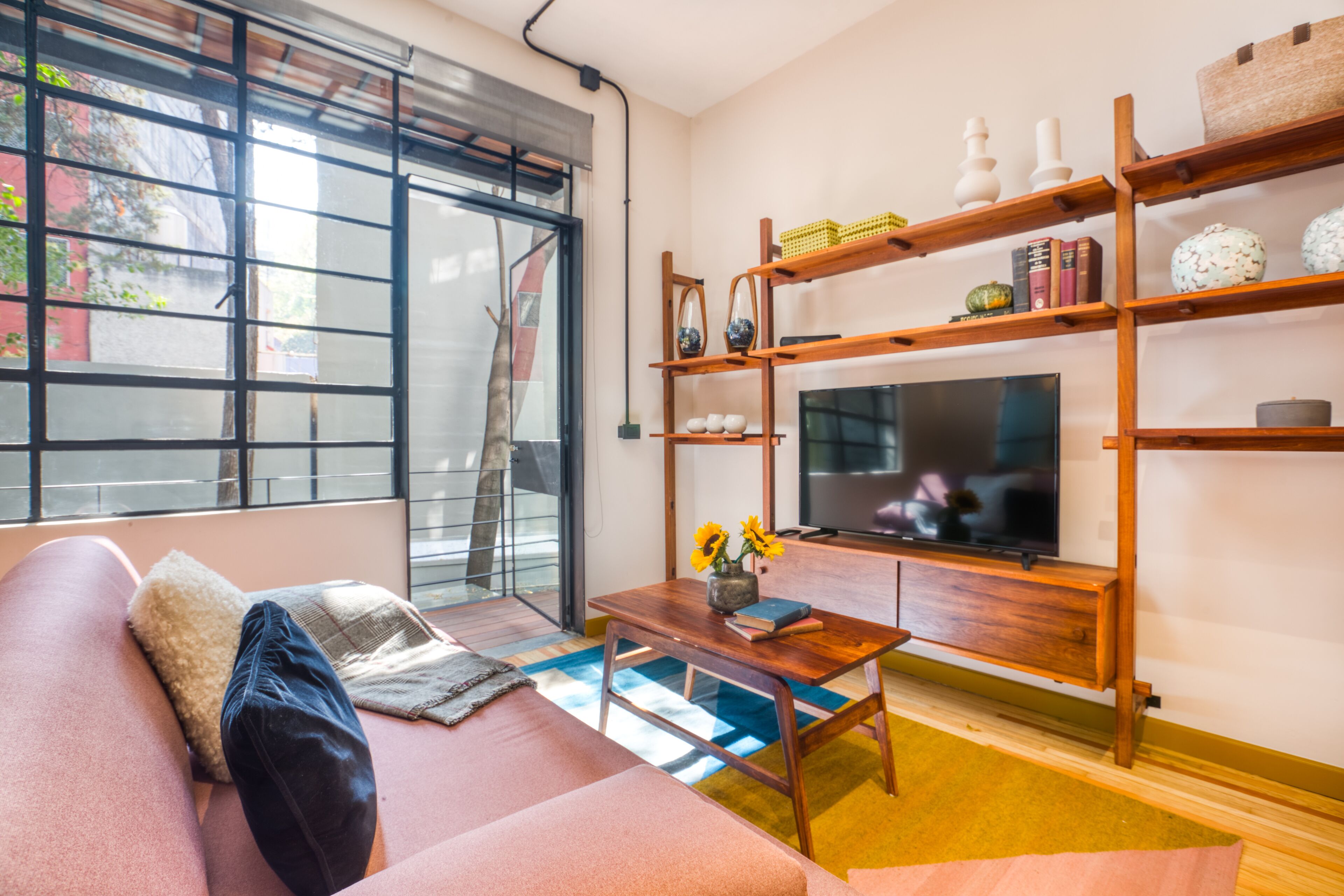 A living room with a sofa, a coffee table, a TV, and wooden shelves with decorative items.