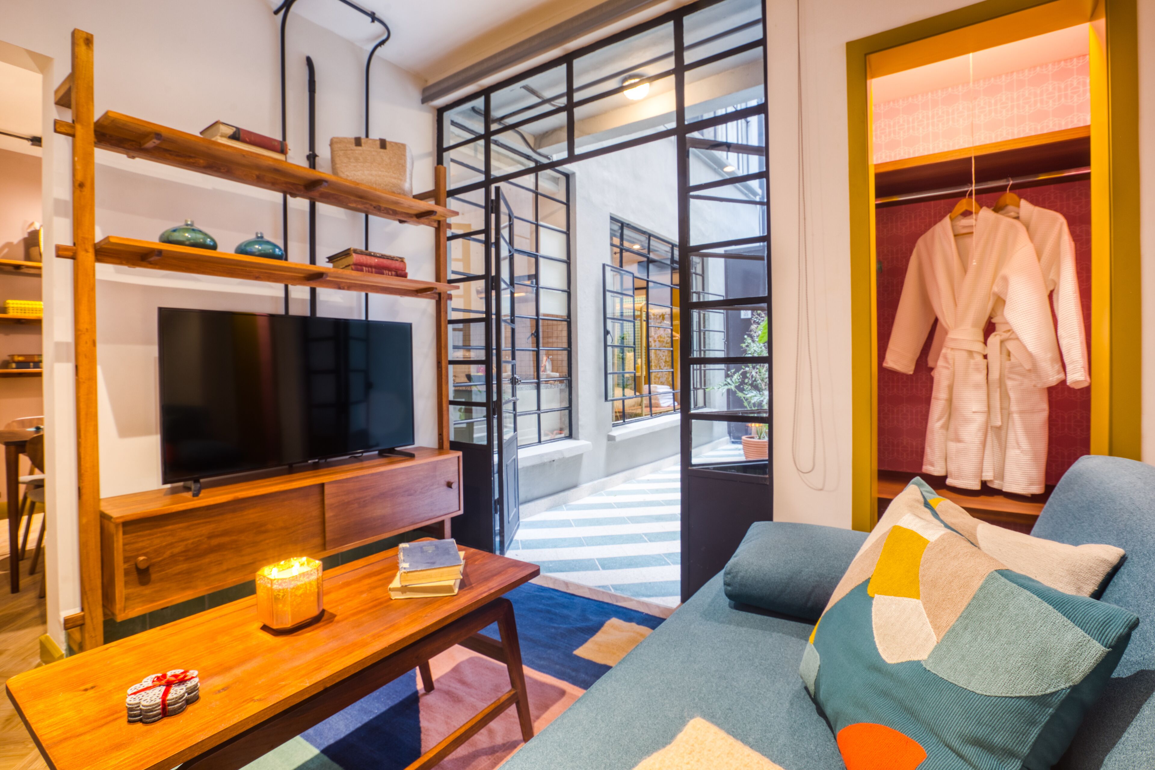 A modern living room with a television, wooden shelves, a sofa, and a clothing rack.