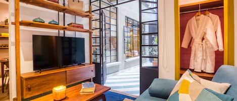 A modern living room with a television, wooden shelves, a sofa, and a clothing rack.