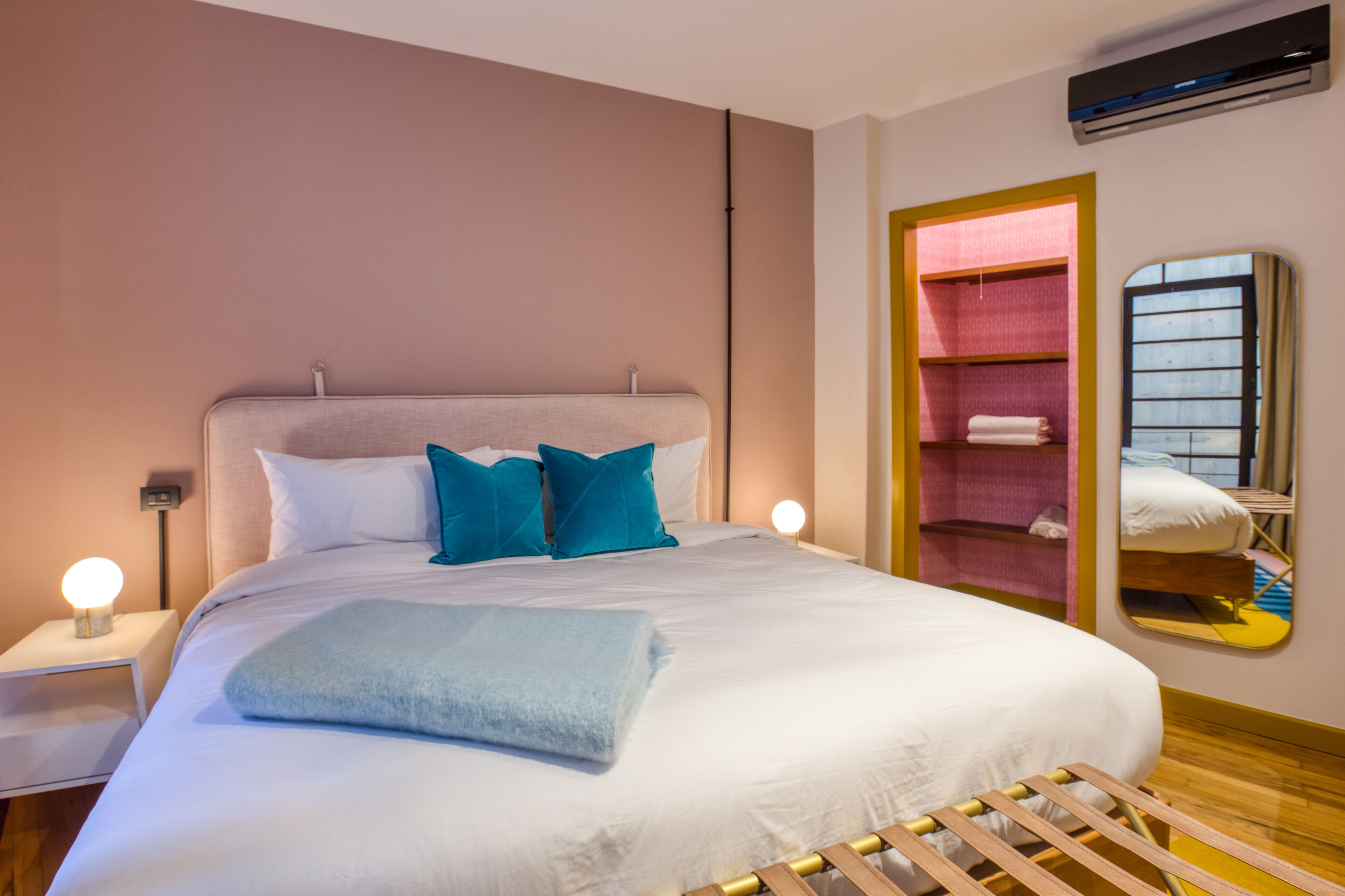 A neatly made bed with white and blue bedding, a bedside lamp, and a mirror reflecting the room.