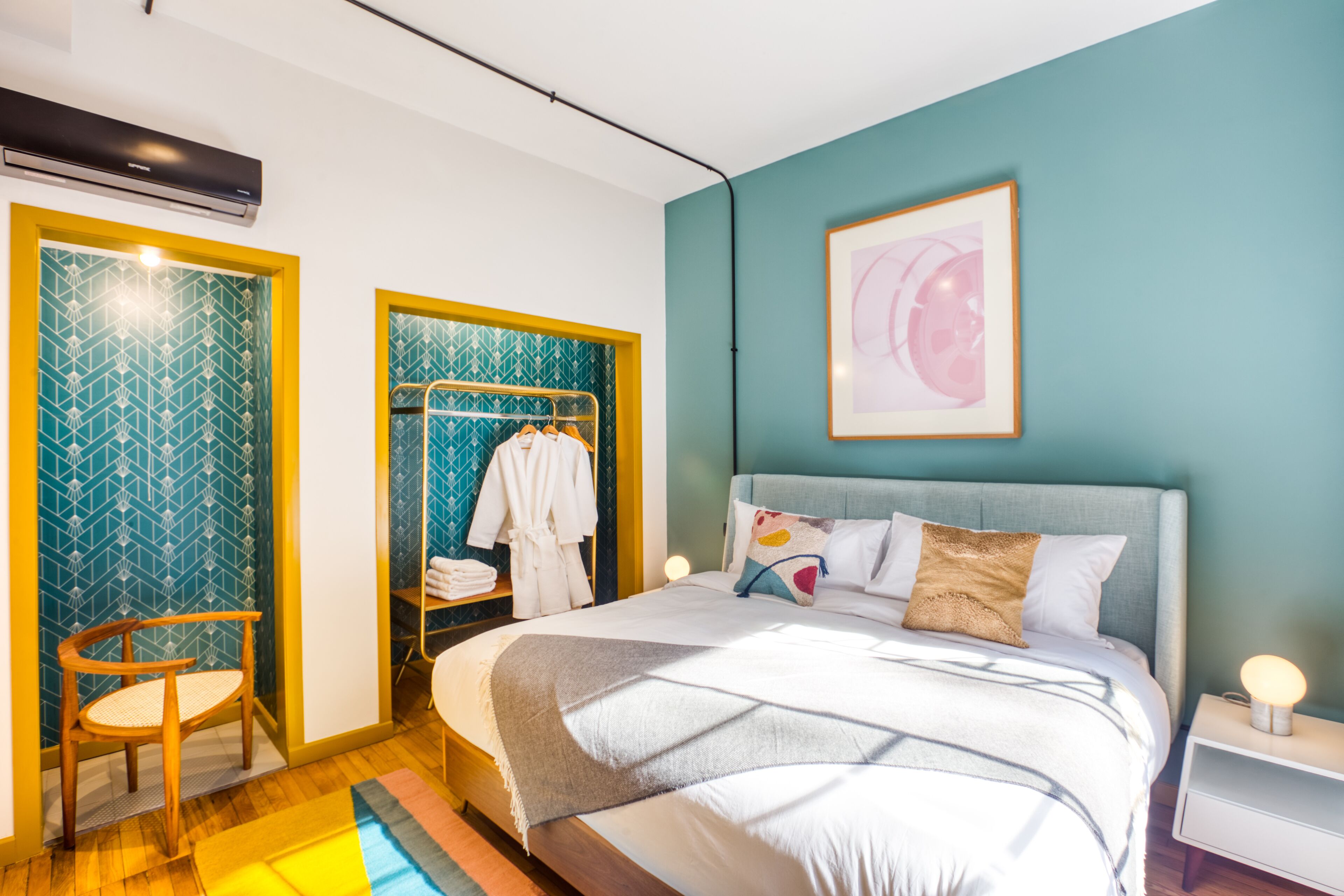 A bedroom with a bed, a nightstand, a chair, a wardrobe, and a framed picture on the wall.