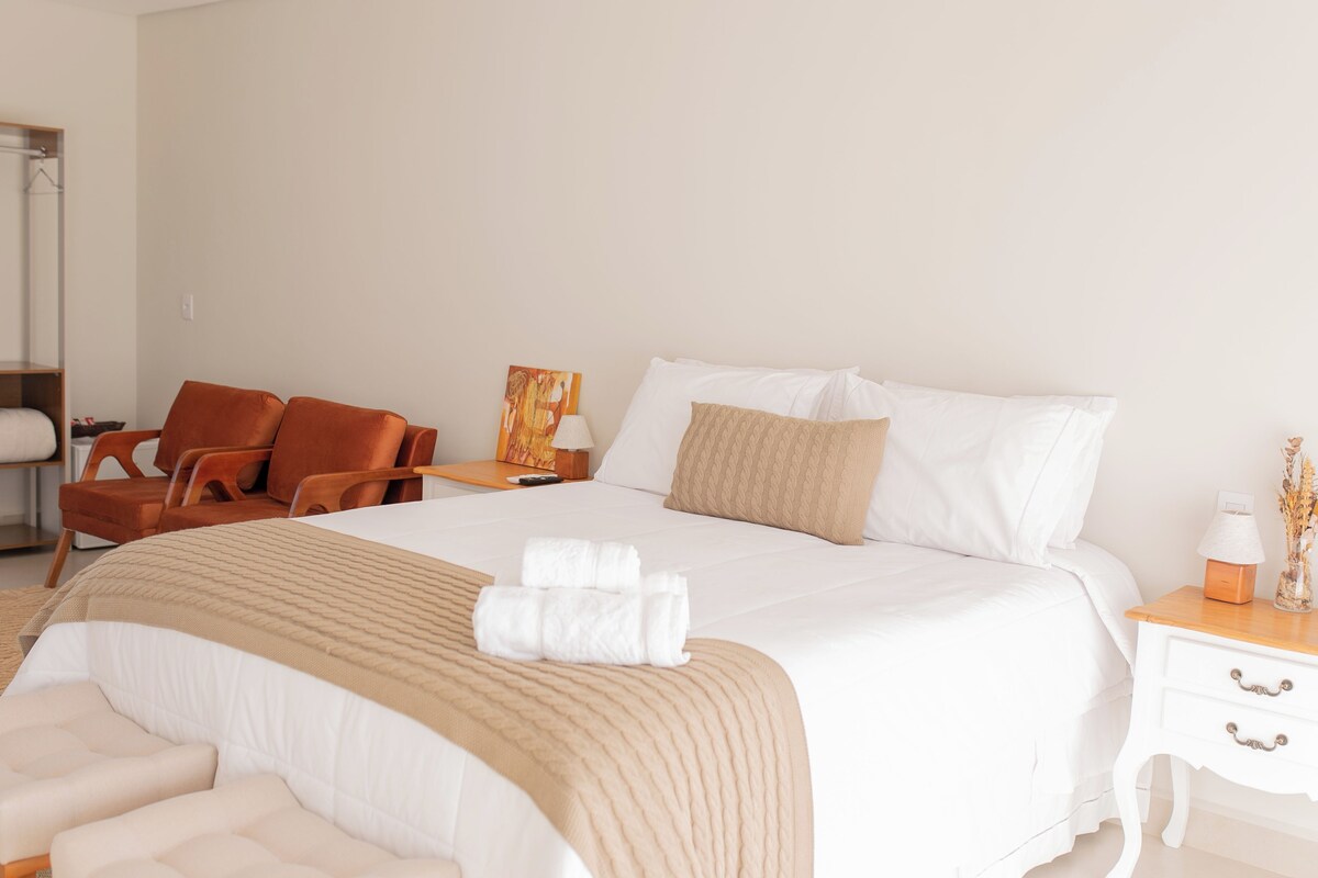 A hotel room with a large bed, a wooden chair, a nightstand, and a wardrobe.