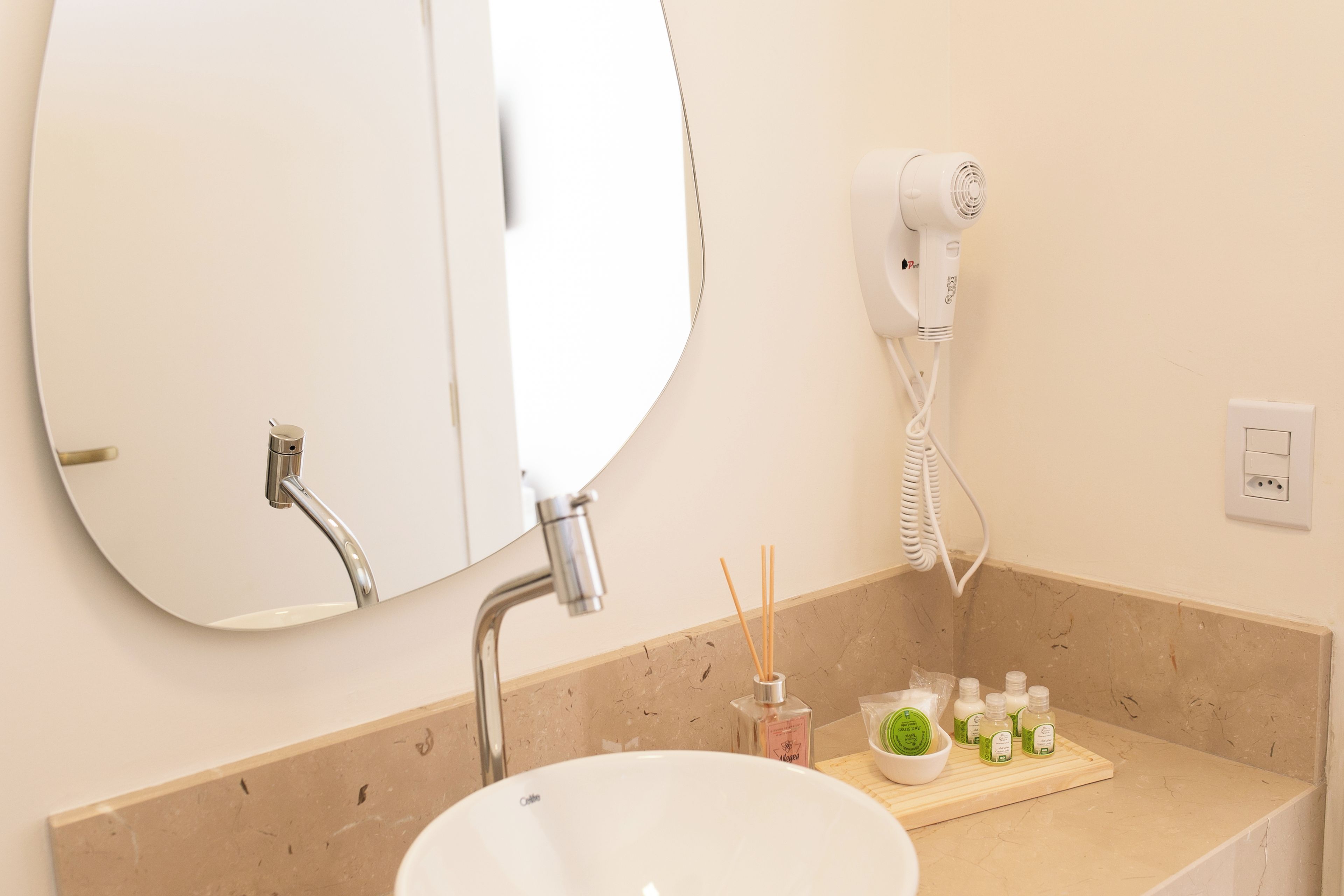 A bathroom with a round mirror, a sink, a hairdryer, and a tray with toiletries.