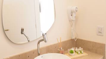 A bathroom with a round mirror, a sink, a hairdryer, and a tray with toiletries.