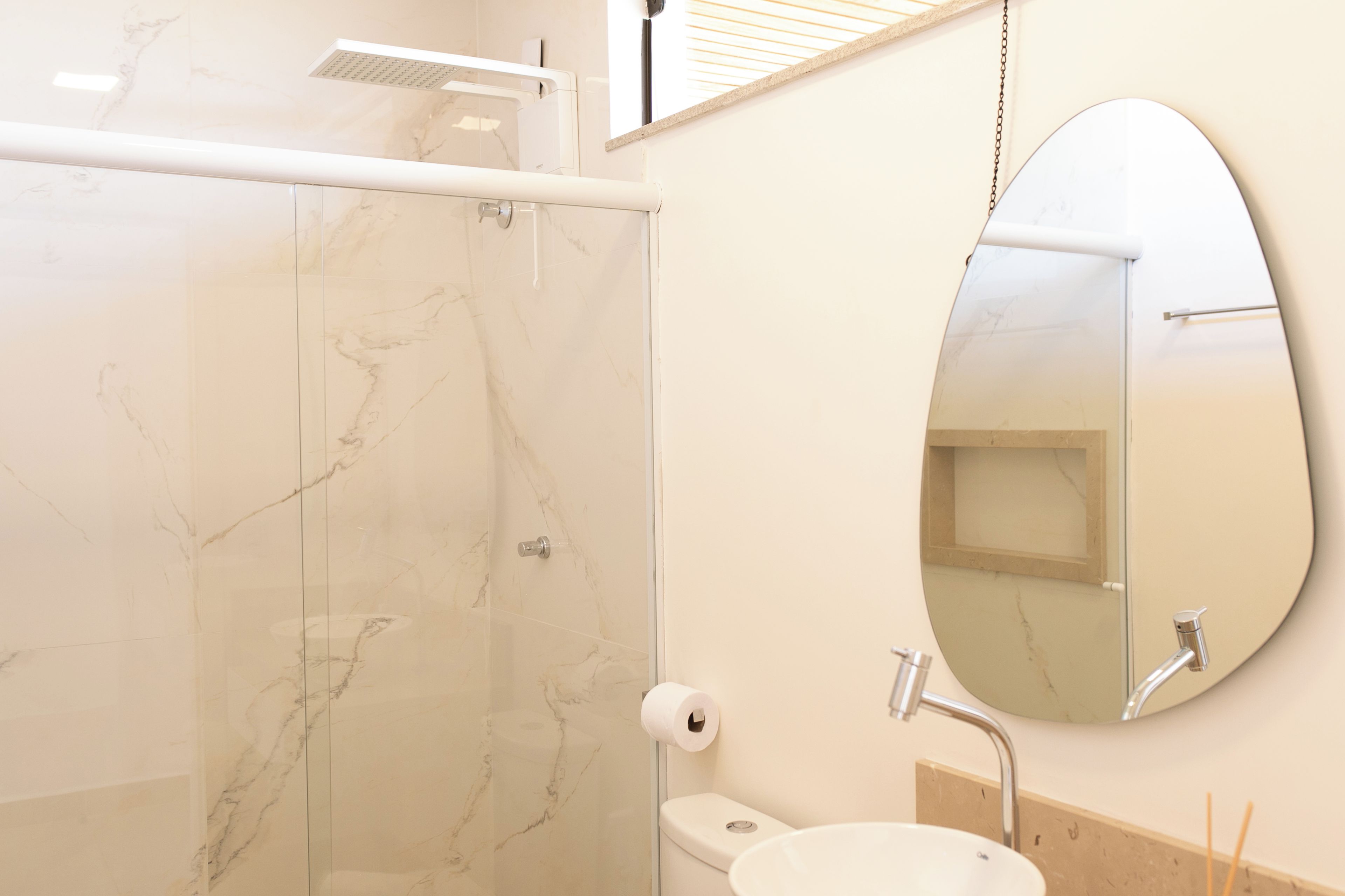 A bathroom with a glass shower enclosure, a toilet, a sink, and a mirror.