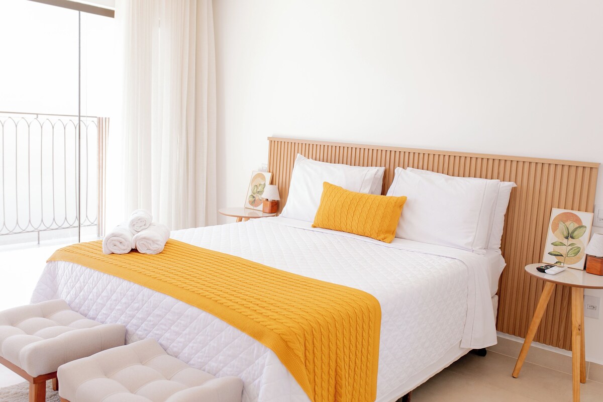 A hotel room with a bed, a bedside table, a chair, and a view of the outdoors.