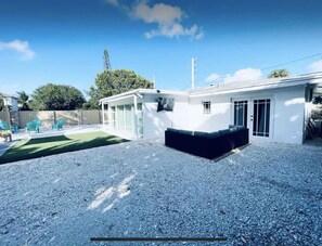 A white building with a covered patio area, a gravel driveway, and a fenced backyard.