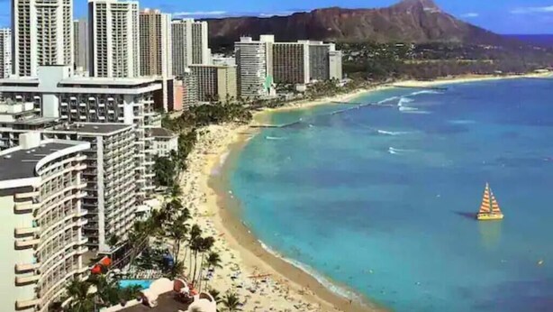 A coastal cityscape with high-rise buildings, a beach, and a sailboat. - Waikiki Ocean View Deluxe Studio (Honolulu)
