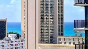 A high-rise building with multiple balconies, a clear view of the ocean, and a modern architectural design. - Waikiki Ocean View Deluxe Studio (Honolulu)