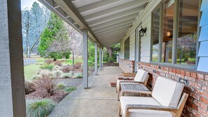 A covered outdoor seating area with brick walls and large windows, overlooking a landscaped garden. - Fishing & Rafting Retreat: 7 Mi to Rogue River! (Grants Pass)