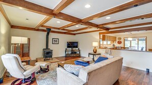 A spacious living room with a large sofa, a recliner, and a television. There is a kitchen area with wooden cabinets and a dining table. - Fishing & Rafting Retreat: 7 Mi to Rogue River! (Grants Pass)