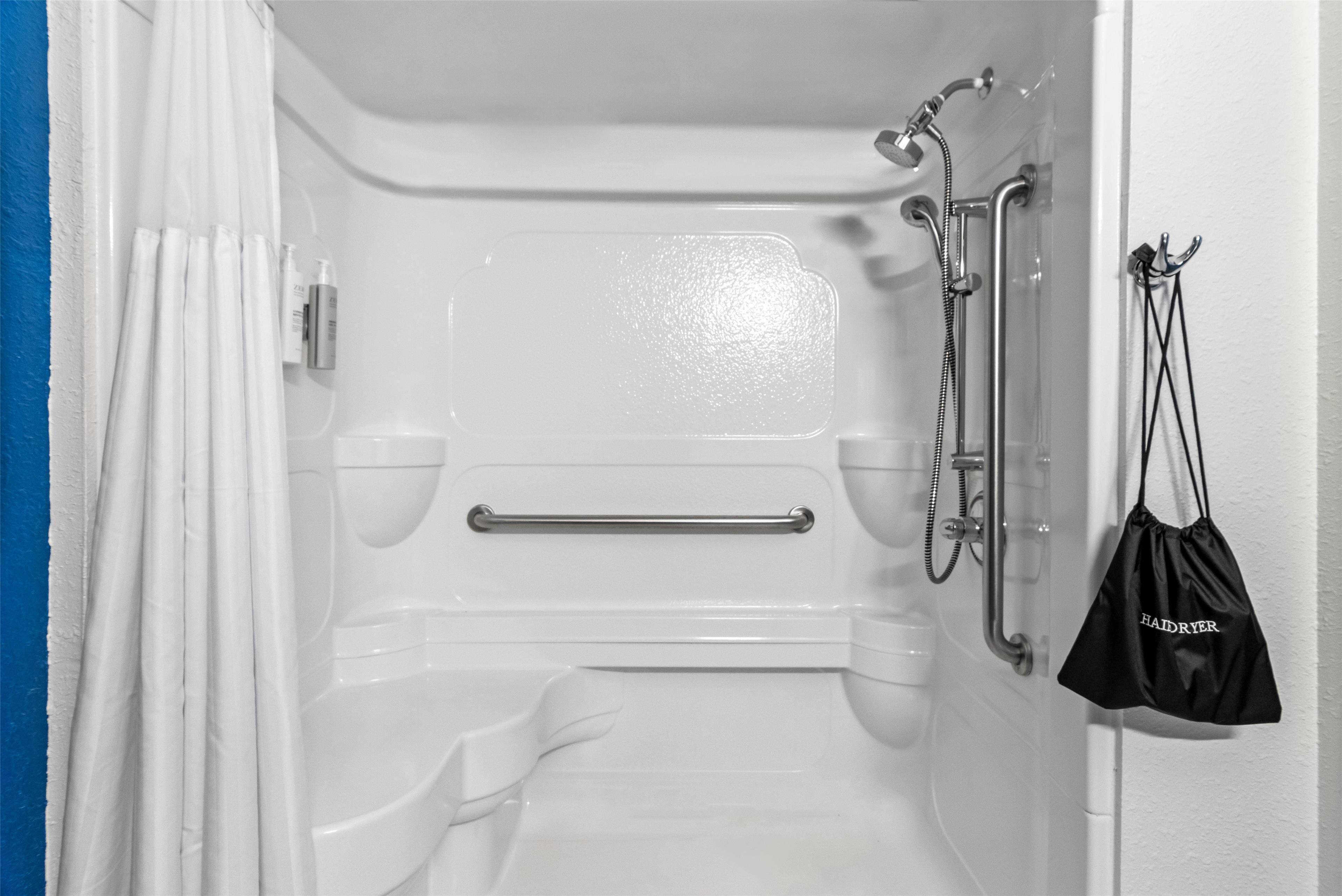 A bathroom with a shower, grab bar, and a hairdryer bag hanging on the wall.
