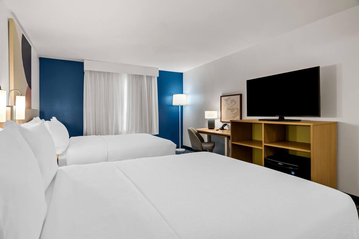 A hotel room with two beds, a desk, a television, and a lamp.