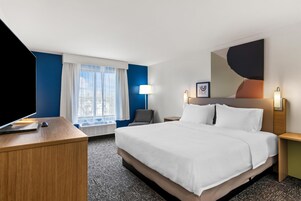 Habitación de hotel con una cama grande, un escritorio con ordenador, una silla, una ventana con cortinas y un cuadro en la pared.