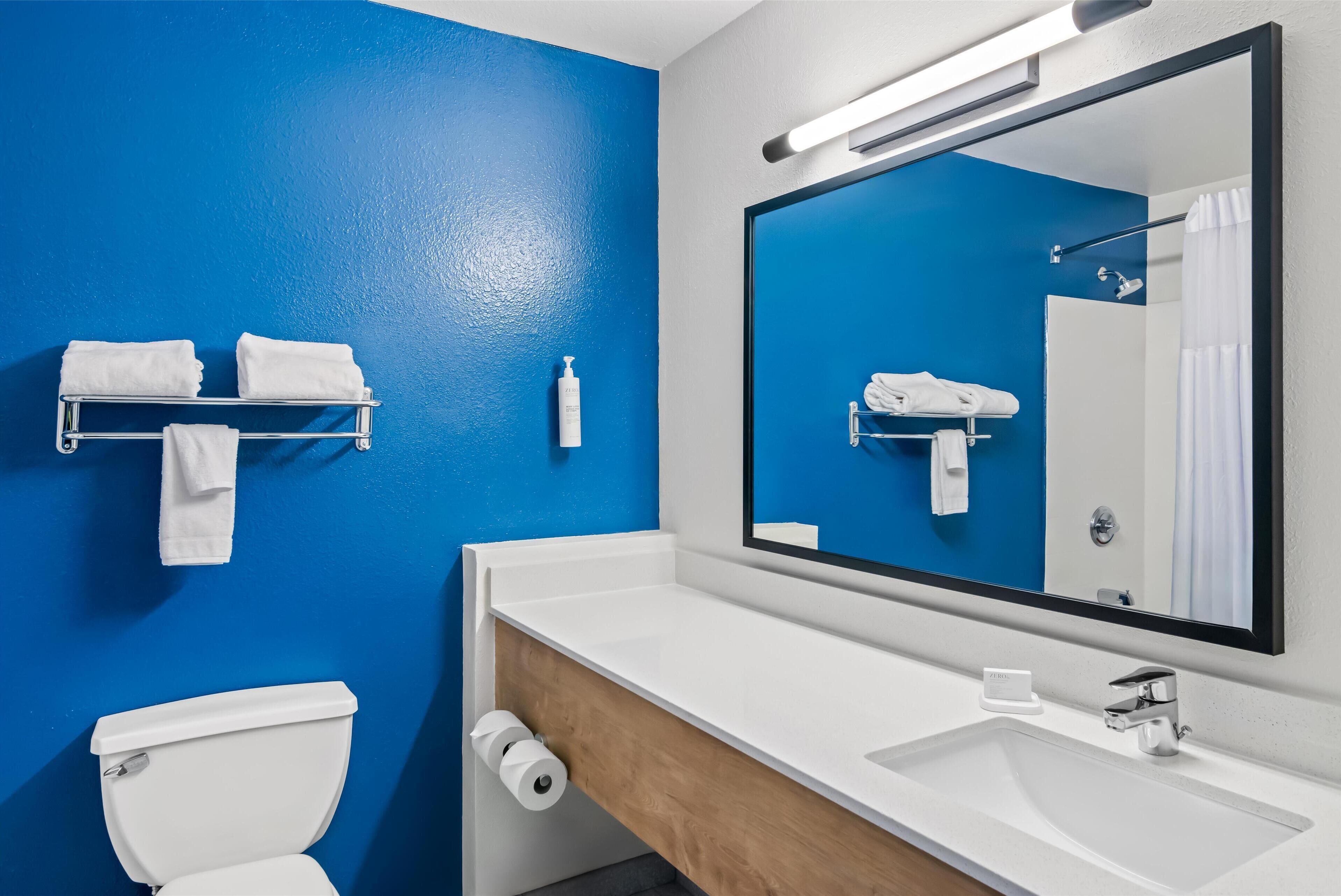 A bathroom with a blue wall, white fixtures, a large mirror, and a towel rack.